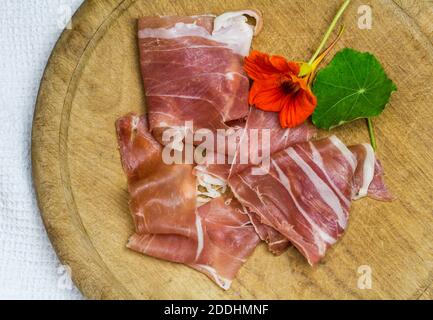 Prosciutto crudo Scheiben auf rustikalem Holzbrett mit Kaperblume Und Lamelle - Draufsicht Bild mit Kopierraum Stockfoto