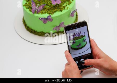 Mädchen mit schwarzen Nägeln macht Bilder von einem appetitlichen Kuchen Auf einem weißen Hintergrund auf ihrem Smartphone Stockfoto