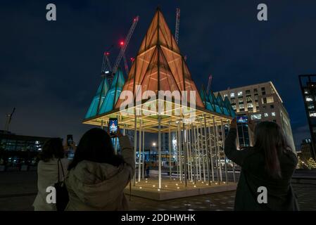 London, Großbritannien. 25. November 2020. Besucher sehen den Electric Nemeton Tree, von Sam Jacob Studio, auf dem Granary Square, der einer von drei ‘traditionell untraditionellen’ Weihnachtsbäumen ist, die jetzt in King’s Cross ausgestellt werden. Die 36 Fuß hohe Struktur bezieht sich auf alte keltische Haine genannt Nemetons, die unter Verwendung der natürlichen Landschaft gebaut wurden und als heilige Sammelplätze fungierten. Alle drei Bäume sind während der Weihnachtszeit bis zum 4. Januar 2021 zu sehen. Kredit: Stephen Chung / Alamy Live Nachrichten Stockfoto