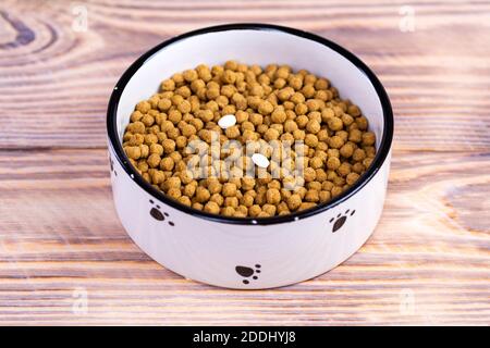 Katzenfutter mit zwei Tabletten in einer Schüssel auf dem Boden. Vitamine für Katzen. Behandlung von Katzen Stockfoto