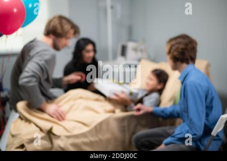 Eine verschwommene Aufnahme einer Familie, die ein Geburtstagskind in einem Krankenhaus besucht. Stockfoto