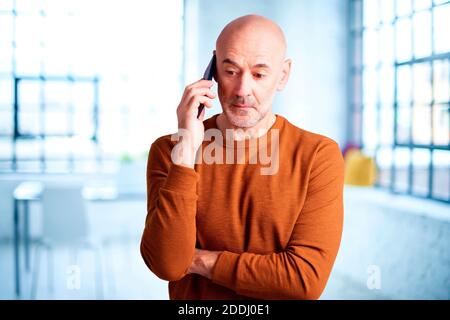 Aufnahme eines Mannes mit überraschendem Gesicht, der einen Anruf macht, während er im Wohnzimmer steht. Stockfoto