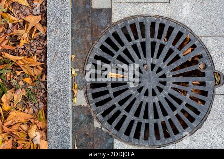 Schachtabdeckung rund schwarz Metallgitter auf einem Stadtpark Fußgängerweg gepflastert mit Granit grauen Fliesen mit einer Steingrenze Nahaufnahme von oben Ansicht, niemand Stockfoto