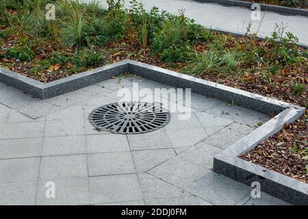 Schachtabdeckung rund schwarz Metallgitter auf einem Stadtpark Fußgängerweg gepflastert mit Granit grauen Fliesen mit einem Stein Grenze Nahaufnahme Blick Herbst Meere Stockfoto