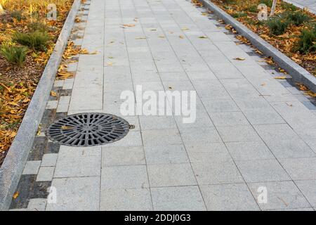 Schachtabdeckung rund schwarz Metallgitter auf einem Stadtpark Fußgängerweg gepflastert mit Granit grauen Fliesen mit einem Stein Grenze Nahaufnahme Blick Herbst Meere Stockfoto