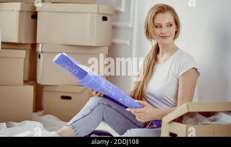 Mädchen sitzt zwischen Boxen macht Marken auf dem Plan der Wohnung Stockfoto