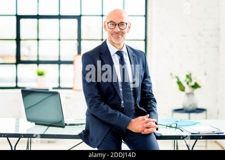 Porträtaufnahme eines leitenden Geschäftsmanns, der Anzug und Krawatte trägt, während er am Schreibtisch sitzt. Stockfoto