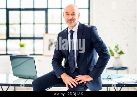 Porträtaufnahme eines leitenden Geschäftsmanns, der Anzug und Krawatte trägt, während er am Schreibtisch sitzt. Stockfoto