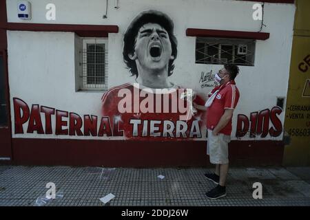 Buenos Aires, Argentinien. November 2020. Ein Fan im 10-Mann-Trikot des Argentinos Juniors steht mit Blumen vor einem Wandbild mit dem Bild des im Alter von 60 Jahren verstorbenen Diego Mardona. Der dribbelnde Künstler wuchs in ärmlichen Verhältnissen am Stadtrand von Buenos Aires auf und wurde schon in jungen Jahren vom First Division Club Argentinos Juniors entdeckt. Quelle: Gustavo Ortiz/dpa/Alamy Live News Stockfoto