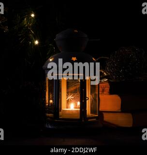Weiße Laterne mit brennender Kerze. Bücher, Weihnachtsbaum Zweig und Lichter auf dem Hintergrund. Nachtdunkles Bild. Weihnachten Mystery Stimmung. Stockfoto