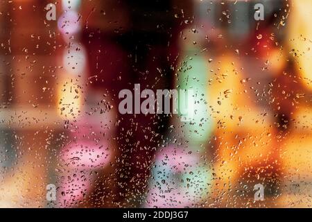 Nasses Glas Fenster mit Regentropfen, verschwommenes Straßenbokeh. Abstrakter, unscharfer, farbenfroher Hintergrund. Konzept von Wetter, Jahreszeiten, Stadt bei Nacht Stockfoto