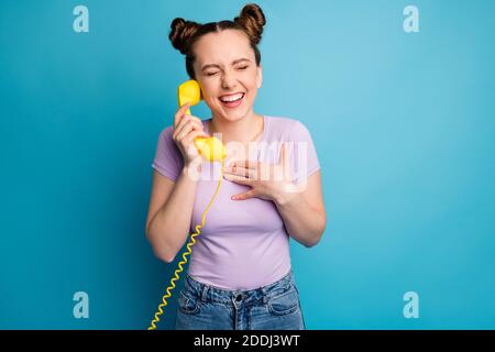 Foto von ziemlich aufgeregt funky Dame zwei Brötchen halten Kabel Telefon Hörer sprechen chatten Freunde diskutieren frische Gerüchte lachen tragen Lässiges Lila Stockfoto