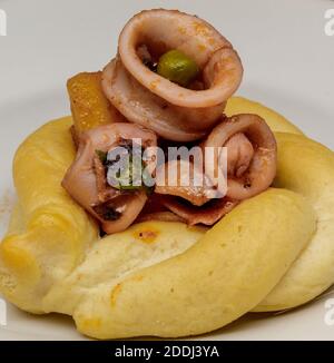 Geschmorte Calamari mit Erbsen, Kartoffeln, Zwiebeln, Petersilie, Tomaten, Pfeffer, Salz, Öl und Zitronenschale auf knusprigem Brot. Stockfoto