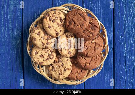 Kekse mit Schokolade und Nüssen in Korbteller auf blauem Holzhintergrund, Draufsicht Stockfoto