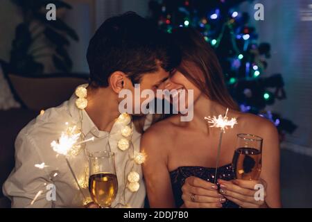 Weihnachts- und Neujahrsparty. Liebespaar brennende Wunderkerzen von beleuchteten Weihnachtsbaum mit Champagner. Stockfoto