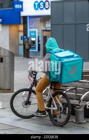 deliveroo Delivery Rider auf einem Push-Bike oder Fahrrad wartet auf Benachrichtigung über eine Bestellung zu sammeln und an eine Adresse zu liefern. Stockfoto