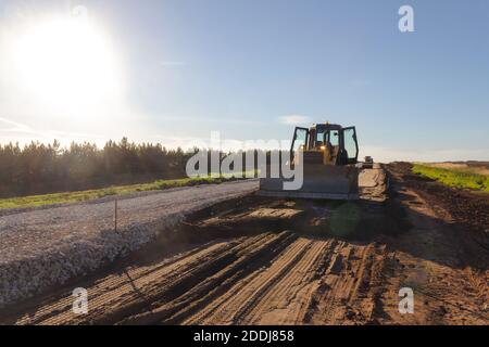 Planierraupe während der Straßenbauarbeiten. Baumaschinen. Erde bewegt sich durch einen Bulldozer in den Bau einer Straße. Bagger auf einer Konstruktion sitzen Stockfoto