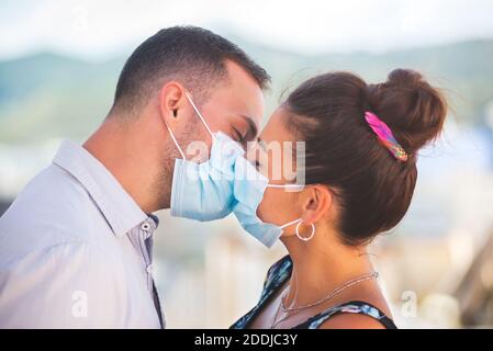 Ein Mann und eine Frau küssen sich mit Coronavirus Schutzmasken Stockfoto
