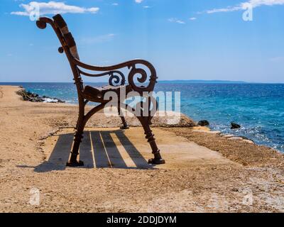 Leere Bank. Eine Bank an der Promenade am Meer. Sommer, sonnig. Schattierungen von Gelb und Blau. Stockfoto