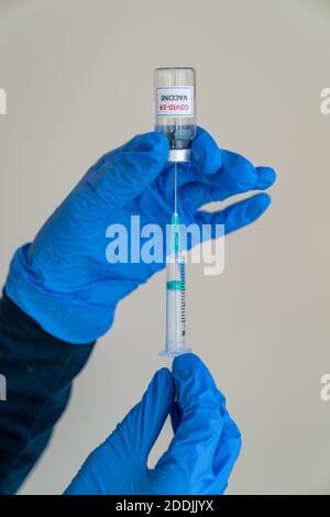 Ärztin oder Krankenschwester trägt blaue Latexhandschuhe Zeichnung ein Dosis des COVID-19-Impfstoffes in eine Spritze von einem Medizinische Glasfläschchen für flüssige Immunisierung Stockfoto