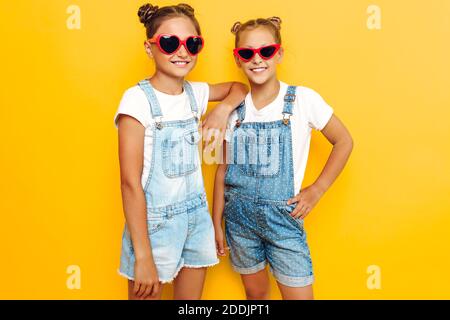 Zwei Teenager-Mädchen, stilvolle Freundinnen in Sonnenbrillen posiert auf einem gelben Hintergrund Stockfoto