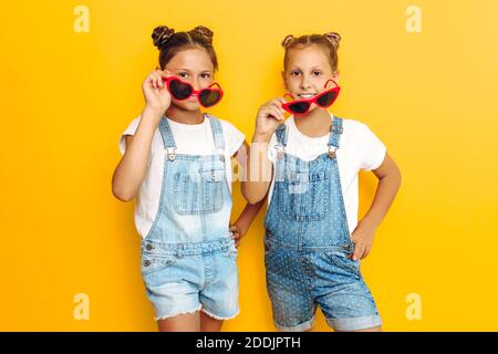 Zwei Teenager-Mädchen, stilvolle Freundinnen in Sonnenbrillen posiert auf einem gelben Hintergrund Stockfoto