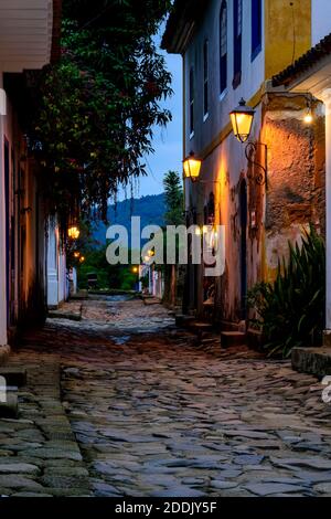 Dämmerung Blick auf die Stadt Paraty mit seinen alten Kolonialstil Häuser, Laternen und die Helligkeit und Farben der Stadt Lichter in der gepflasterten reflektiert Stockfoto