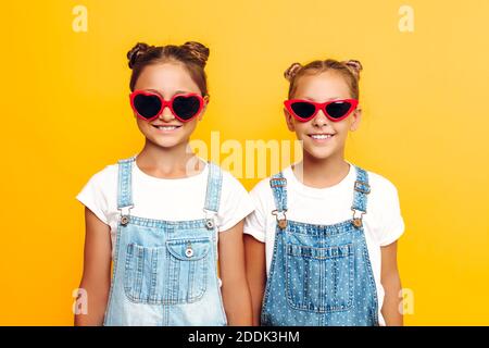 Zwei Teenager-Mädchen, stilvolle Freundinnen in Sonnenbrillen posiert auf einem gelben Hintergrund Stockfoto