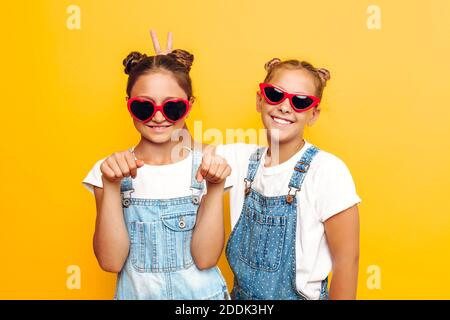 Zwei Teenager-Mädchen, stilvolle Freundinnen in Sonnenbrillen posiert auf einem gelben Hintergrund Stockfoto