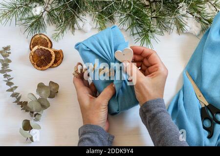 Weibliche Hände Verpackung mit Liebe Weihnachtsgeschenke. Handgemachte Geschenkbox Verpackung in blauem Tuch in japanischer furoshiki-Stil. Dekorierter Wohntisch, Blick von oben Stockfoto