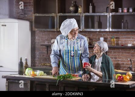 Seniorenpaar kocht zusammen. Der Mann trägt Kochmütze und hackt frisches Gemüse. Gesunde Ernährung habbits. Stockfoto