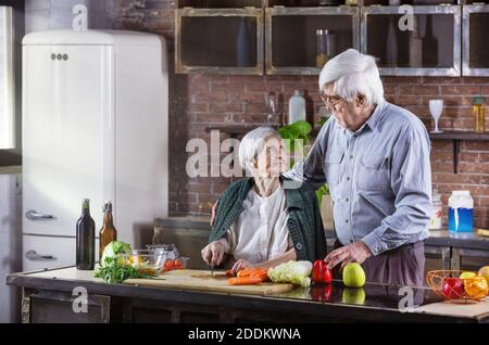 Reifer Mann und seine Mutter kochen zusammen. Seniorenpaar bereitet Essen in der Küche zu. Frau hackt Gemüse. Stockfoto