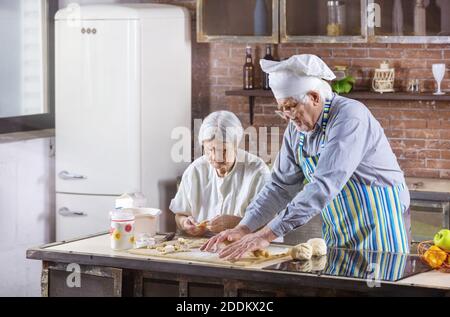 Seniorenpaar bereitet Gebäck in der Küche zu Hause. Der Mann trägt einen Kochhut. Stockfoto