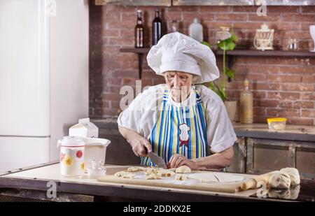 Ältere Frau im Chefkoch hat Gebäck in der Küche zubereitet Zu Hause Stockfoto