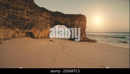 Cliff einzigartige Wand mit riesigen Loch bei Sonnenlicht aeial. Sandstrand an Ocean Bay Wellen. Niemand Natur szenische Seestück. Felsküste der Sumba Insel, Indonesien. Tropisches Paradiesresort im Kino Stockfoto