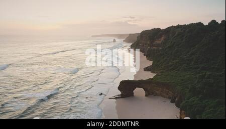 Sonnenaufgang an der Küste der Ozeanklippe mit Blick auf ein riesiges Loch an der Felswand. Tropische Natur Landschaft des Paradieses Sandstrand und grünes Gras felsigen Küste. Touristenattraktion der Insel Sumba Stockfoto