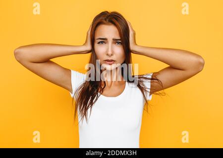 Nahaufnahme einer depressiven jungen Frau, mit schrecklichen Kopfschmerzen, die ihre Schläfen mit ihren Händen berühren, auf einem gelben Hintergrund Stockfoto
