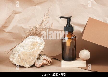 Braune Glasflasche mit Pumpe von kosmetischen Produkten auf Holz geometrischen Formen, Steinen und getrockneten Blumen auf beigem Papier Hintergrund. Natürliches Organisches Spa Stockfoto