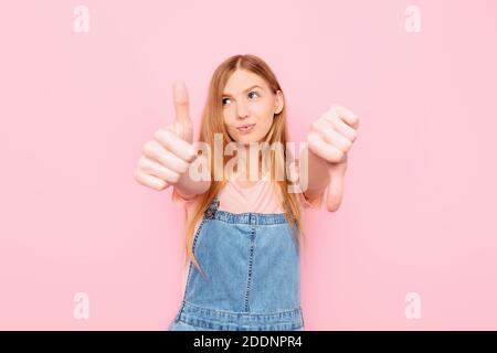 Eine junge attraktive stilvolle Frau macht ein gut-schlecht Zeichen. Unentschieden zwischen Ja oder Nein, auf einem isolierten rosa Hintergrund Stockfoto