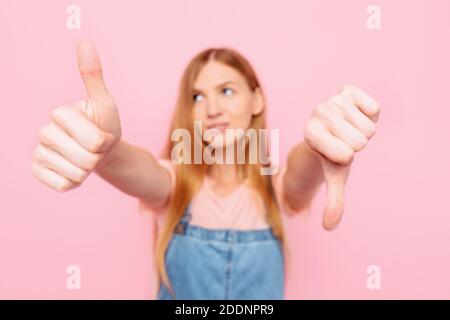 Eine junge attraktive stilvolle Frau macht ein gut-schlecht Zeichen. Unentschieden zwischen Ja oder Nein, auf einem isolierten rosa Hintergrund Stockfoto