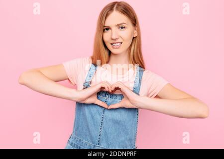 Eine schöne junge Frau in der Liebe bildet mit ihren eigenen Händen ein Herz, auf einem isolierten rosa Hintergrund Stockfoto