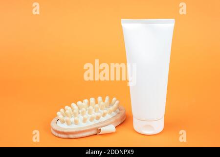 Weiße leere Kosmetiktube mit Creme oder Körperlotion und Anti-Cellulite-Massagegerät aus Holz auf orangefarbenem Hintergrund. Konzept Kampf gegen Cellulite. Mockup Fro Stockfoto