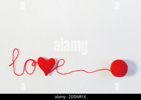 Valentinstag oder Hochzeit im Hintergrund. Rot gestricktes Volumen Herz im Wort Liebe und Ball aus Faden auf weißem gestrickten Hintergrund. Vorlage für Design, VA Stockfoto