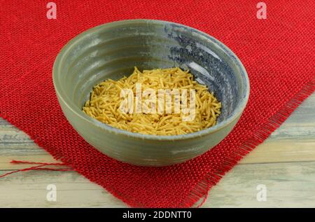 Knusprige indische Besan Sticks Snack in Keramik Schüssel auf rot Tuch auf dem Tisch Stockfoto