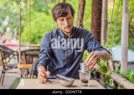 Kaukasischen Mann und traditionelle Tropfen gebrühten vietnamesischen Kaffee aus phinfilter Stockfoto