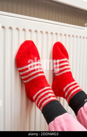 Ein Mädchen in roten Wollsocken wärmt ihre Füße an Den Kühler Stockfoto