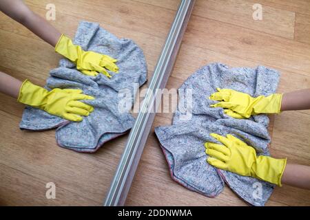 Mädchen in Gummihandschuhen wäscht den Boden zu Hause in der Nähe des Spiegels mit einem Lappen. Konzept der Hausarbeit und Housekeeping Stockfoto