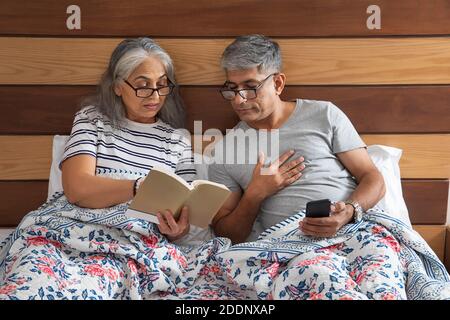 Ein älteres Paar sitzt im Bett und liest und tauscht Notizen aus Stockfoto