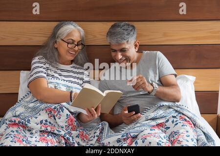 Ein älteres Paar sitzt im Bett und liest und tauscht Notizen aus Stockfoto