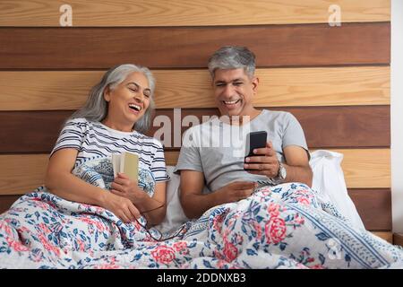 Ein älteres Paar sitzt im Bett und liest und teilt ein Licht Moment Stockfoto